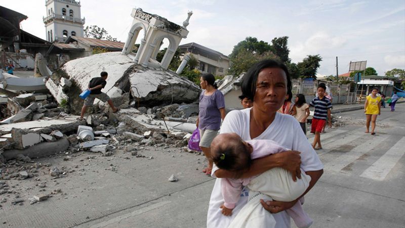 बोहोल में गिरे चर्च से अपने बच्चे को दूर ले जाती महिला। यही द्वीप भूकंप के झटकों का केंद्र था।