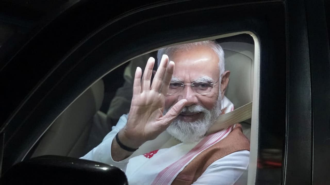 Prime Minister Narendra Modi waves during the roadshow, in Guwahati on Saturday. (@CMOfficeAssam/ANI Photo) Prime Minister Narendra Modi waves during the roadshow, in Guwahati on Saturday. (@CMOfficeAssam/ANI Photo)