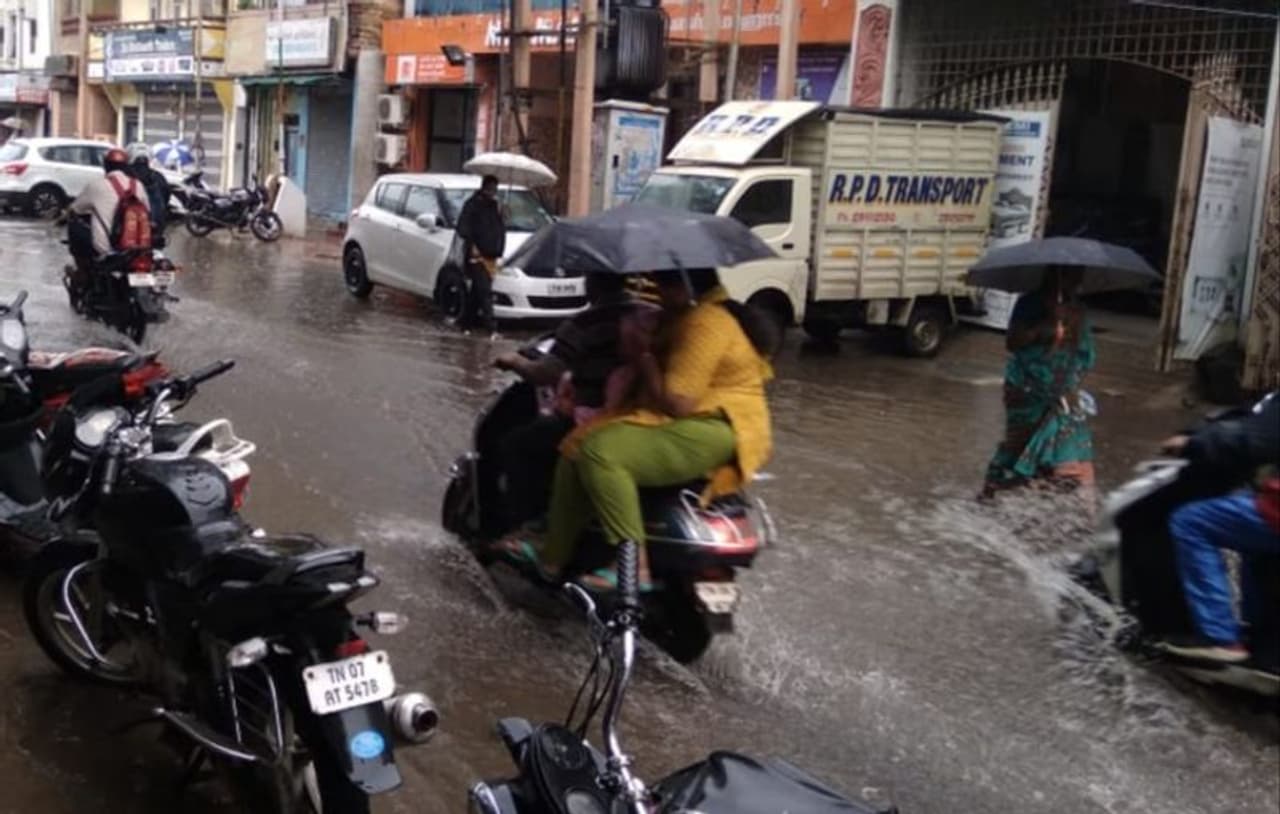 வண்டியில் செல்லும் போது மழையில் நனையாமல் குடைபிடித்து செல்லும் பெண் வண்டியில் செல்லும் போது மழையில் நனையாமல் குடைபிடித்து செல்லும் பெண்