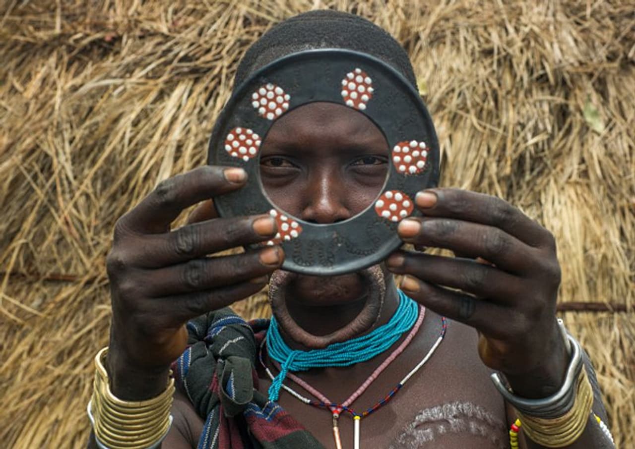 <p>വെറും 12 വയസ്സ് മാത്രം ഉള്ളപ്പോൾ പെൺകുട്ടികളുടെ ചുണ്ട് ഒരു മുള്ളുകൊണ്ട് ഉയർത്തി ബ്ലേഡ് ഉപയോഗിച്ച് മുറിക്കുന്നു. ഇത് അവർക്കിടയിൽ അഭിമാനകരമായ ഒരു കാര്യമാണ്. ലിപ് പ്ലഗുകൾ എന്നറിയപ്പെടുന്ന ഈ ലിപ് പ്ലേറ്റുകൾ ഗോത്രവർഗക്കാർക്കിടയിൽ സൗന്ദര്യം വർദ്ധിപ്പിക്കുമെന്ന് കരുതപ്പെടുന്നു. വലിയ കളിമൺ പ്ലേറ്റുകൾ ധരിക്കുന്നതിനായി പല സ്ത്രീകളും അവരുടെ താഴത്തെ നിരയിലെ പല്ലുകൾ നീക്കം ചെയ്യുന്നു. </p> <p>വെറും 12 വയസ്സ് മാത്രം ഉള്ളപ്പോൾ പെൺകുട്ടികളുടെ ചുണ്ട് ഒരു മുള്ളുകൊണ്ട് ഉയർത്തി ബ്ലേഡ് ഉപയോഗിച്ച് മുറിക്കുന്നു. ഇത് അവർക്കിടയിൽ അഭിമാനകരമായ ഒരു കാര്യമാണ്. ലിപ് പ്ലഗുകൾ എന്നറിയപ്പെടുന്ന ഈ ലിപ് പ്ലേറ്റുകൾ ഗോത്രവർഗക്കാർക്കിടയിൽ സൗന്ദര്യം വർദ്ധിപ്പിക്കുമെന്ന് കരുതപ്പെടുന്നു. വലിയ കളിമൺ പ്ലേറ്റുകൾ ധരിക്കുന്നതിനായി പല സ്ത്രീകളും അവരുടെ താഴത്തെ നിരയിലെ പല്ലുകൾ നീക്കം ചെയ്യുന്നു. </p>