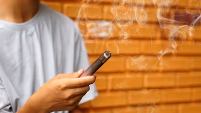 Male teenager holds a smoked e-cigarette in his hand