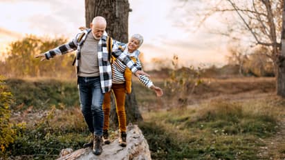 Senior couple walking on a tree log in forest