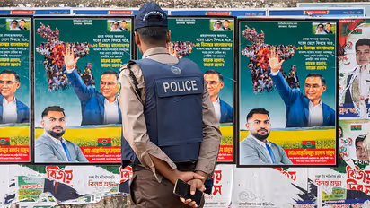 A police officer stands facing a wall covered with campaign placards depicting Tarique Rahman, the Chairman of the Bangladesh Nationalist Party (BNP).