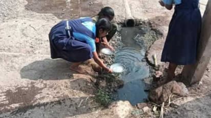 Students washing mid-day meal plates near a drain at a govt school