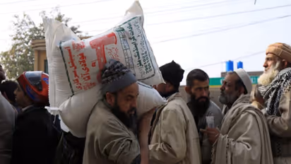 A man carries sacks of flour on his shoulder, while others stand in queue to purchase from a truck ( File Photo/ Reuters)