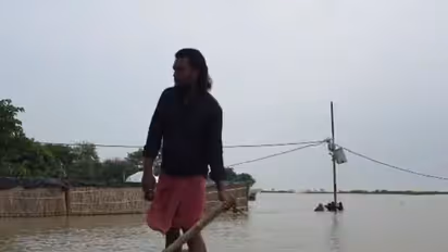 A man navigates a small boat through a flooded area near submerged houses and power lines (Photo/ANI)