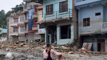 A woman speaks on a phone as she sits next to a gas cylinder at the site of flash floods and mudslides, in Devighat (File Photo/ANI)